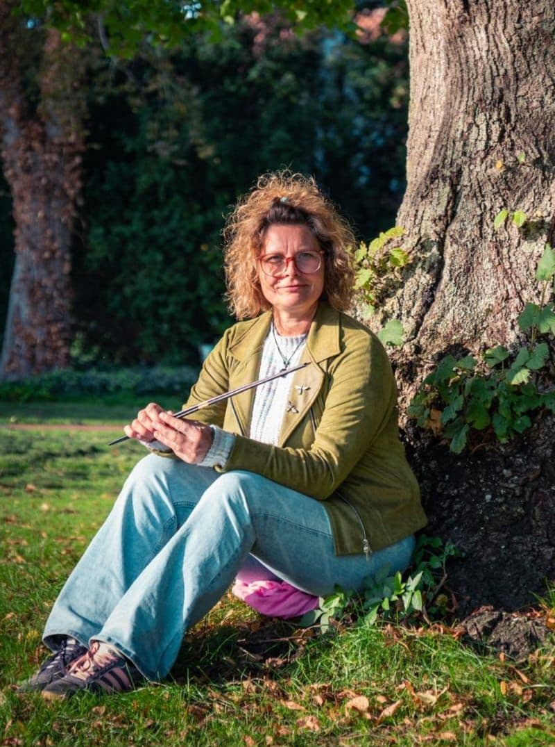 Marion Röttger sitzt in der Natur und hält eine Rute in den Händen